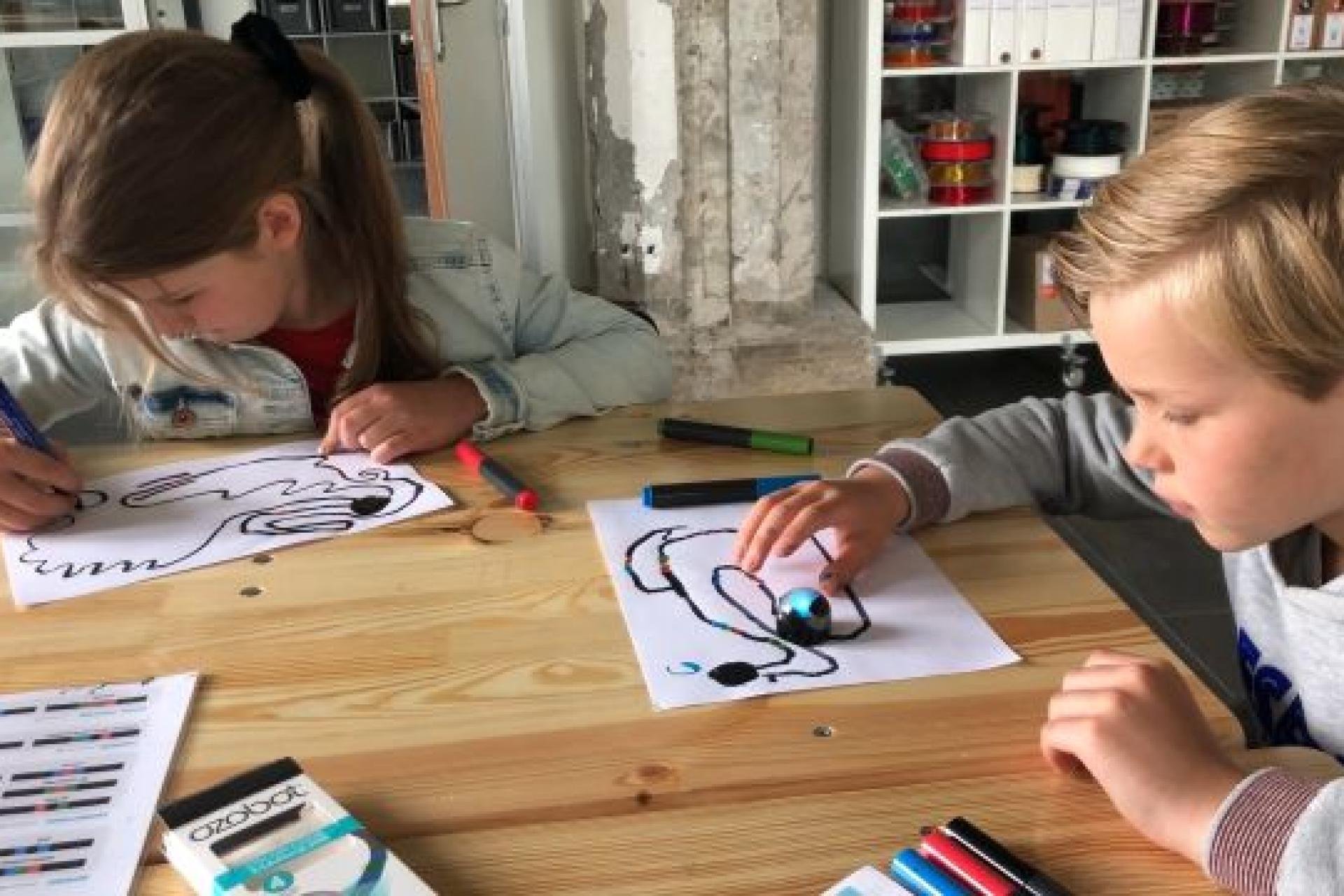 2 kinderen aan tafel die lijnen op papier aan het maken zijn voor robot Ozobot